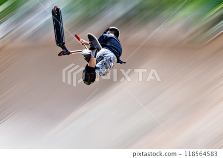 Young man practicing Scootering (Freestyle Scootering) in the new SkatePark in the central park of Igualada, Barcelona, Spain. blurred background 118564583