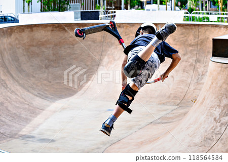 Young man practicing Scootering (Freestyle Scootering) in the new SkatePark in the central park of Igualada, Barcelona, Spain. blurred background Young man practicing Scootering (Freestyle Scootering) in the new SkatePark in the central park of Igualada, Barcelona, Spain. blurred background 118564584