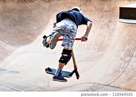 Young man practicing Scootering (Freestyle Scootering) in the new SkatePark in the central park of Igualada, Barcelona, Spain. blurred background 118564585