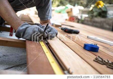Worker with protective gloves marking a spot on wooden plank while placing it on a foundation for outside patio 118564783