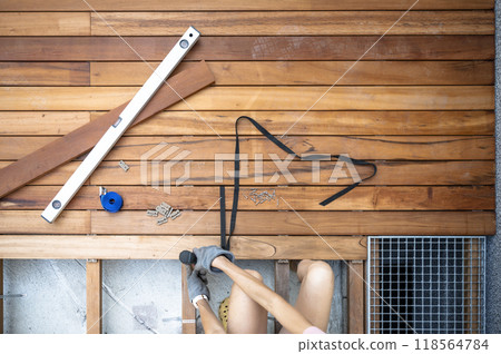 Woman in domestic DIY project - screwing a screw in a wooden plank for a new outdoor patio 118564784
