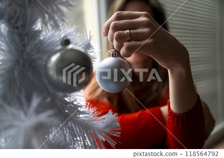 Woman hanging holiday bauble on a christmas tree Woman hanging holiday bauble on a christmas tree 118564792
