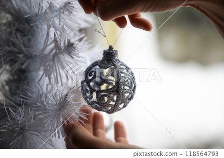 Female hands hanging shiny lace like holiday bauble on a christmas tree Female hands hanging shiny lace like holiday bauble on a christmas tree 118564793