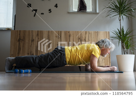 Senior man with grey curly hair in bright yellow tshirt exercising at home making a plank position 118564795