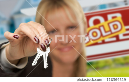 Female Real Estate Agent Presenting House Keys In Front of Sold For Sale Sign & New House. Focus is on the Keys. 118564819