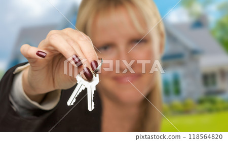 Female Real Estate Agent Presenting House Keys In Front of New House. Focus is on the Keys. 118564820
