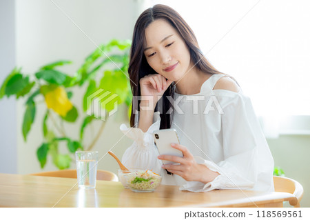 A woman looking at her smartphone during breakfast 118569561