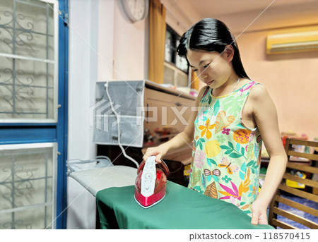 Portrait of Asian child girl is ironing cloth, child practicing ironing at the first time at home. Landscape image with space. Real situation image. Portrait of Asian child girl is ironing cloth, child practicing ironing at the first time at home. Landscape image with space. Real situation image. 118570415