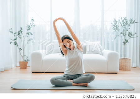 Happy young Asian woman practicing yoga and shoulder stretching at home Happy young Asian woman practicing yoga and shoulder stretching at home 118570825