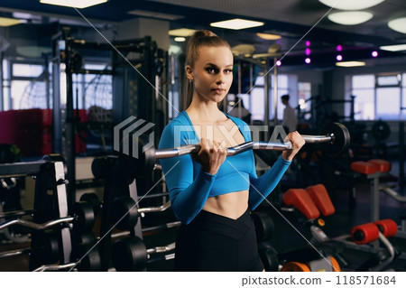 A young woman lifts weights in a modern gym during a fitness session A young woman lifts weights in a modern gym during a fitness session 118571684