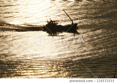 Silhouette of a fishing boat floating in the morning sun Silhouette of a fishing boat floating in the morning sun 118572533