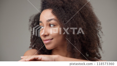 Beauty and healthcare - beautiful African American woman with curly afro hairstyle and clean, healthy skin touching her face, neck, shoulders, looking at the camera with a calm look and a slight smile 118573360
