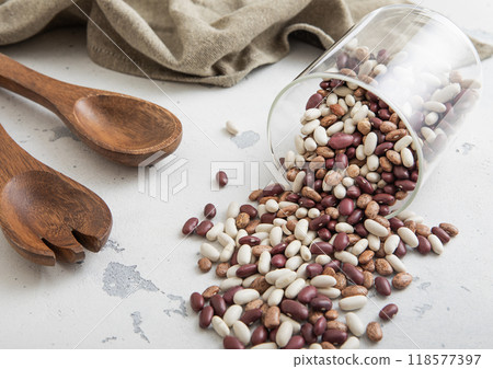 Raw organic variegated beans in glass jar with wooden utensils and kitchen towel on light table.Macro. Raw organic variegated beans in glass jar with wooden utensils and kitchen towel on light table.Macro. 118577397