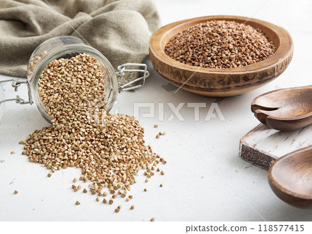 Bowl of brown dry raw organic buckwheat seeds with green seeds in glass jar on light table.Macro. Bowl of brown dry raw organic buckwheat seeds with green seeds in glass jar on light table.Macro. 118577415