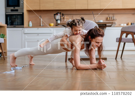 Woman is doing the plank exercise and she has her daughter on her back Woman is doing the plank exercise and she has her daughter on her back 118578202