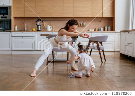 Woman working out at home, doing squats, her daughter plays nearby Woman working out at home, doing squats, her daughter plays nearby 118578203