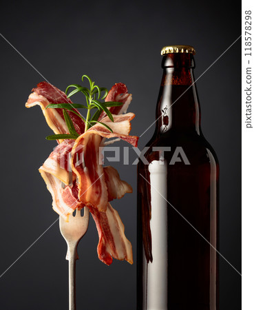 Unopened beer bottle and slices of fried bacon. 118578298