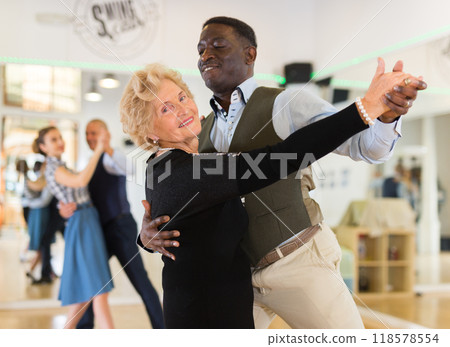 Man and elderly woman performing ballroom dance in dancing room Man and elderly woman performing ballroom dance in dancing room 118578554