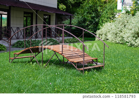 Wooden footbridge over green lawn in backyard garden of residential house. Wooden footbridge over green lawn in backyard garden of residential house. 118581793