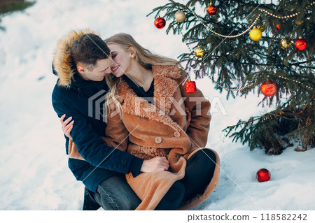 Young adult couple decorates christmas tree in winter forest. New year pine holiday party celebration concept 118582242