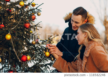 Young adult couple decorates christmas tree in winter forest. New year pine holiday party celebration concept 118582246