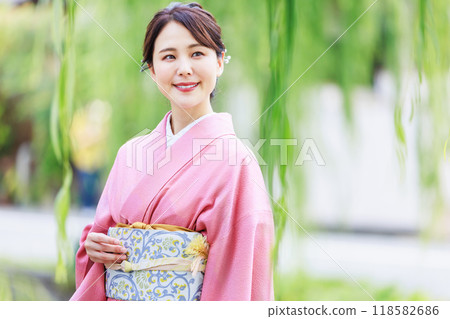 京都白川，一位身穿和服的女子沿著一排柳樹行走 118582686