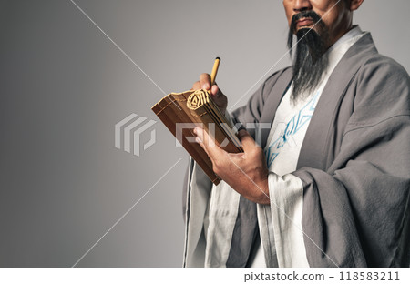 A scene in which a Chinese historical figure, such as Zhuge Liang from the Romance of the Three Kingdoms, writes characters on bamboo slips with a calligraphy brush A scene in which a Chinese historical figure, such as Zhuge Liang from the Romance of the Three Kingdoms, writes characters on bamboo slips with a calligraphy brush 118583211