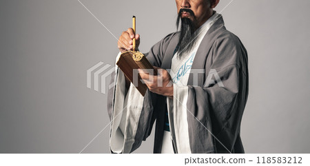 A scene in which a Chinese historical figure, such as Zhuge Liang from the Romance of the Three Kingdoms, writes characters on bamboo slips with a calligraphy brush A scene in which a Chinese historical figure, such as Zhuge Liang from the Romance of the Three Kingdoms, writes characters on bamboo slips with a calligraphy brush 118583212