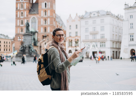 Attractive young female tourist is exploring new city. Happy girl holding a paper map on Market Square in Krakow. Traveling Europe in autumn. St. Marys Basilica 118583595
