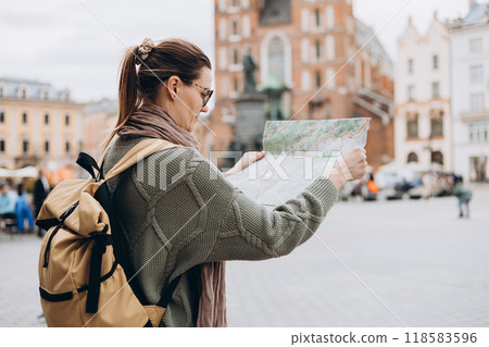 Attractive young female tourist is exploring new city. Happy girl holding a paper map on Market Square in Krakow. Traveling Europe in autumn. St. Marys Basilica 118583596