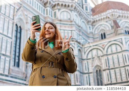 30s girl using smartphone near famous Duomo cathedral in Florence. Happy woman making selfie photo on urban history background. Use technology concept, Traveling Europe in autumn 30s girl using smartphone near famous Duomo cathedral in Florence. Happy woman making selfie photo on urban history background. Use technology concept, Traveling Europe in autumn 118584410
