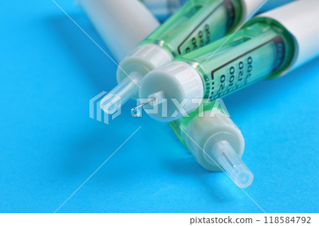 A drop of medicine at the end of a needle of an insulin syringe pen on a blue table 118584792