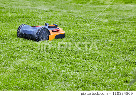 Automatic orange robotic lawn mower on sunny green lawn of park 118584809