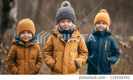 Three young children wearing warm winter clothes walking together outdoors on a cold day 118588392
