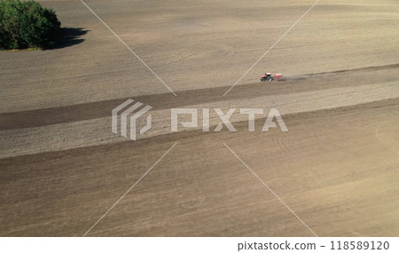 Aerial view of a tractor working on a vast plowed field, preparing the soil for planting 118589120