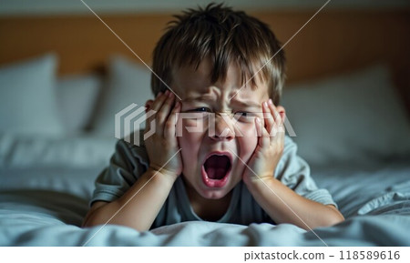 A young boy is laying on a bed, loudly screaming with his mouth wide open 118589616