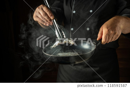 Frying capelin in a frying pan. The chef puts the small fish into the frying pan with kitchen tongs. Menu concept for a restaurant or hotel 118591587