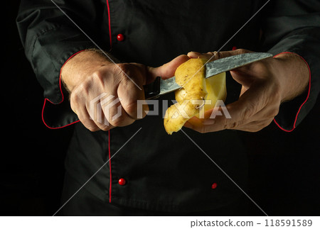 Peeling potatoes with a knife. A chef prepares potatoes for mashing in a hotel or restaurant kitchen. Low key concept for cooking a vegetable dish 118591589