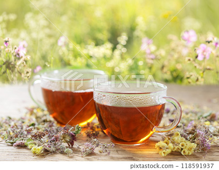 cups of herbal tea and dry flowers on meadow background cups of herbal tea and dry flowers on meadow background 118591937