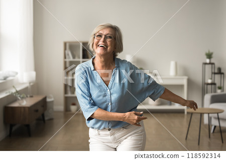Cheerful elderly woman in casual clothes dancing in living room Cheerful elderly woman in casual clothes dancing in living room 118592314