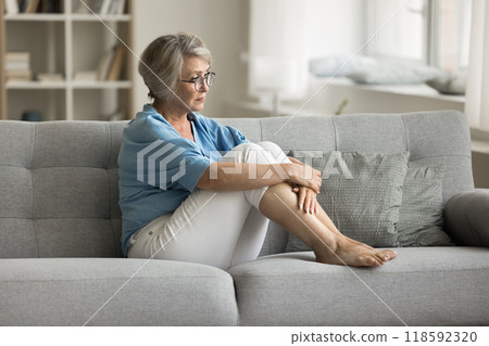Upset mature woman sits on sofa in living room Upset mature woman sits on sofa in living room 118592320