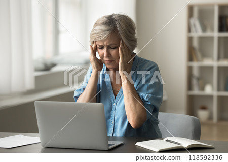 Frowned mature woman experiencing discomfort or pain while using laptop Frowned mature woman experiencing discomfort or pain while using laptop 118592336