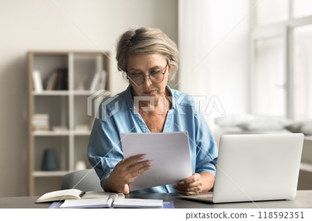 Older woman with serious expression reading document Older woman with serious expression reading document 118592351