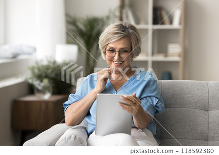 Smiling mature woman sit comfortably on sofa with tablet 118592380