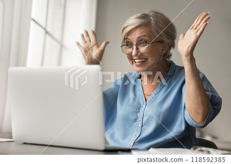 Older woman reading pleasant news raising her hands in excitement Older woman reading pleasant news raising her hands in excitement 118592385