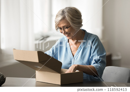 Woman opening cardboard box with look of anticipation and happiness Woman opening cardboard box with look of anticipation and happiness 118592413