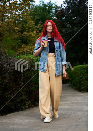 Stylish young woman with red hair walking in park holding coffee cup 118593315