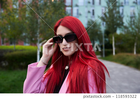 Confident woman adjusts sunglasses while standing in a lush green park Confident woman adjusts sunglasses while standing in a lush green park 118593322