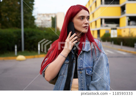 Young woman with red hair uses smartphone on urban street in daylight 118593333