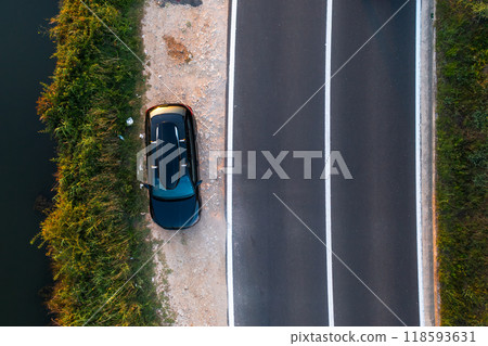 A car parked beside a winding road near a body of water during sunset. A car parked beside a winding road near a body of water during sunset. 118593631